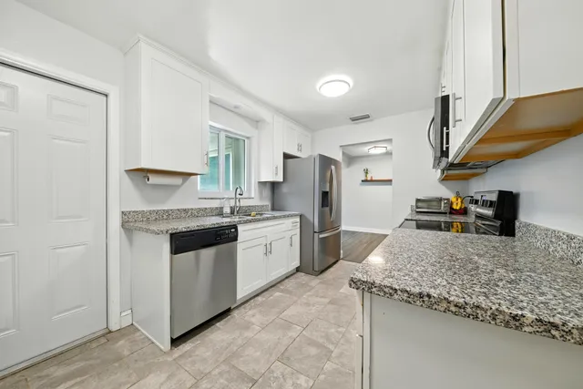 a kitchen with granite countertop a sink stainless steel appliances and white cabinets