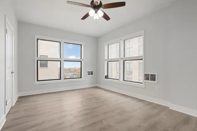 an empty room with wooden floor fan and windows