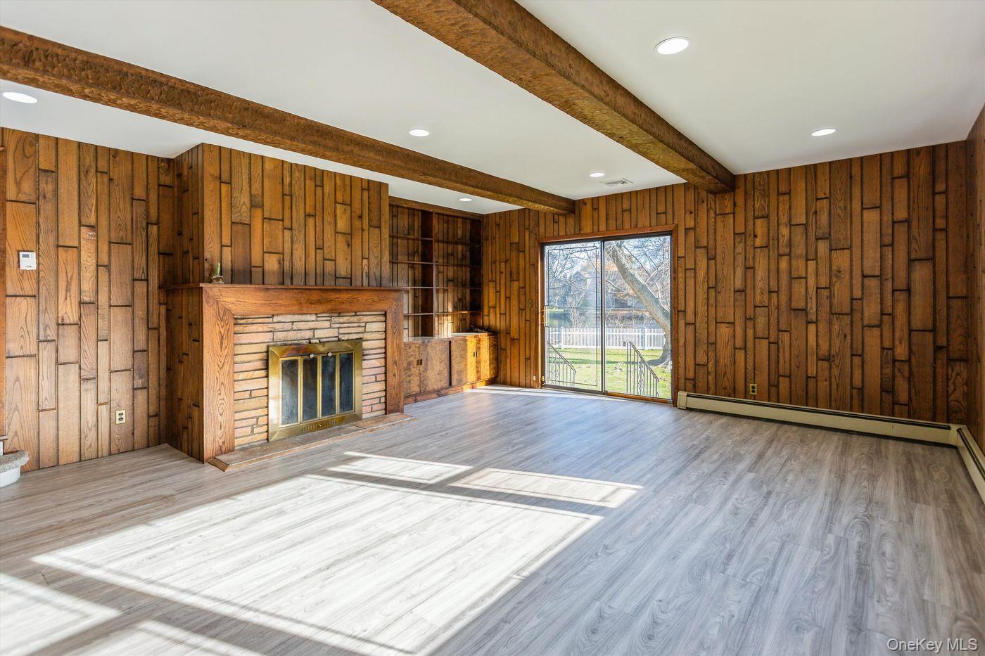 1 Sutton Place Lawrence, NY 11559 - Photo 13 of 38 Unfurnished living room featuring wood walls, beam ceiling, a stone fireplace, recessed lighting, and wood finished floors