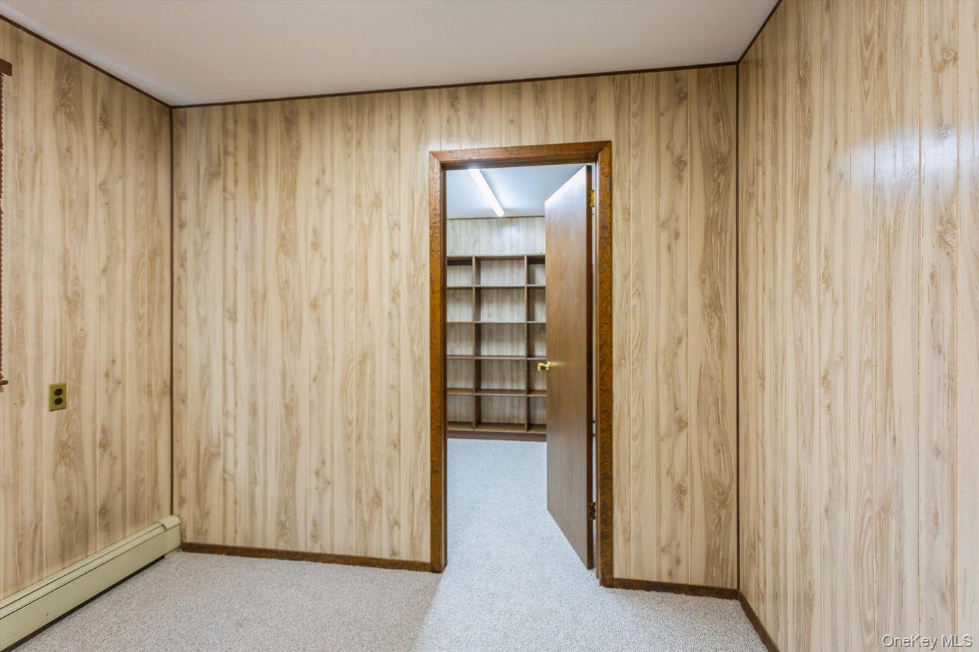 1 Sutton Place Lawrence, NY 11559 - Photo 28 of 38 Spare room with baseboard heating, wood walls, and light carpet