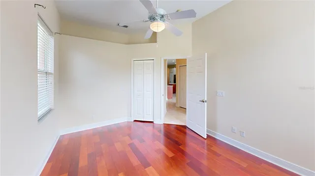 an empty room with wooden floor ceiling fan and windows