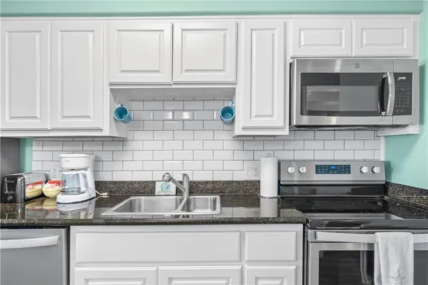 a kitchen with granite countertop white cabinets stainless steel appliances and a counter space