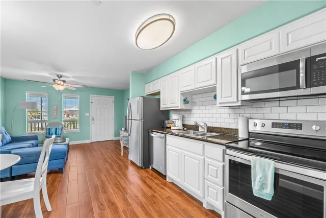 a kitchen with stainless steel appliances granite countertop a stove top oven a sink dishwasher a dining table and chairs with wooden floors