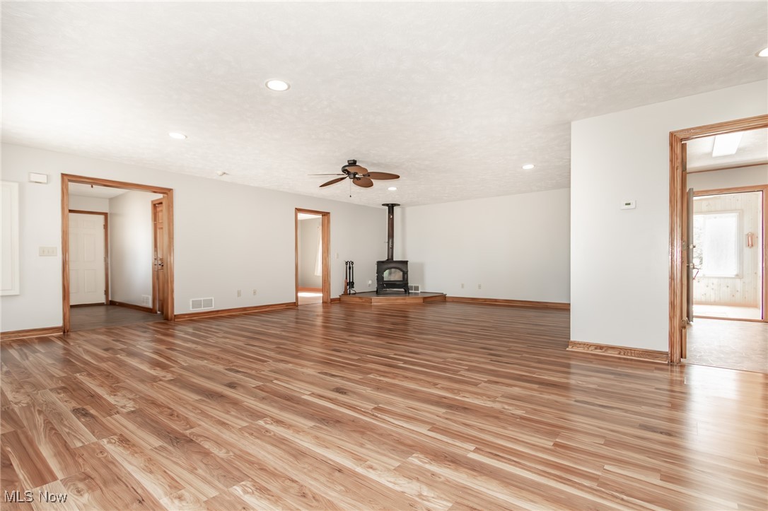 2866 South County Line Road Madison, OH 44057 - Photo 22 of 48 Unfurnished living room featuring a ceiling fan, light wood-style flooring, baseboards, and a wood stove