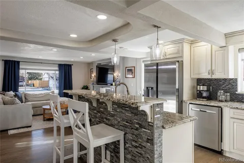 a kitchen with stainless steel appliances kitchen island granite countertop a refrigerator a stove a sink and white cabinets with wooden floor