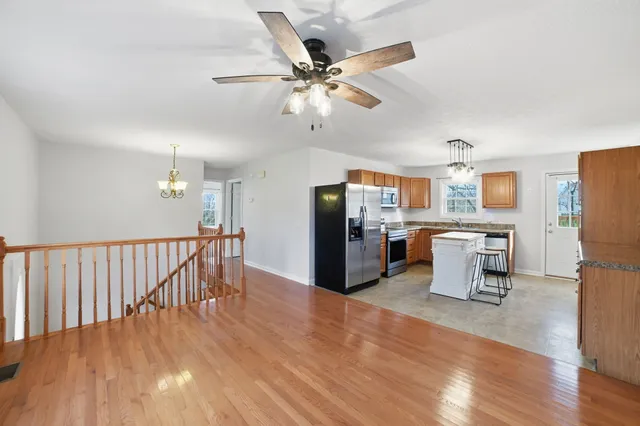 a living room with stainless steel appliances kitchen island hardwood floor and a ceiling fan