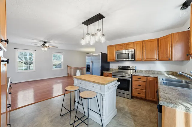 a kitchen with stainless steel appliances granite countertop a stove top oven a refrigerator a sink dishwasher a dining table and chairs with wooden floor