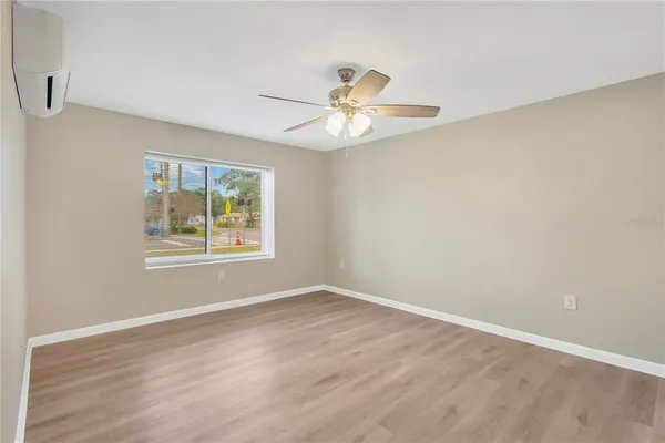 an empty room with wooden floor chandelier fan and windows