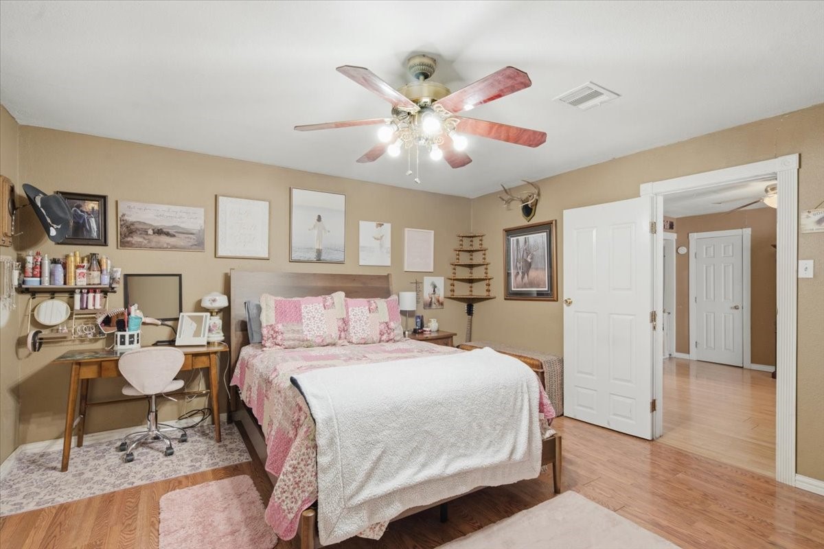 765 Norcross Road Wallis, TX 77485 - Photo 27 of 42 This cozy bedroom features warm-toned walls, wood flooring, and a ceiling fan. The room offers a spacious feel with an open doorway leading to an adjacent area.
