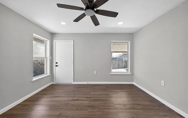 an empty room with wooden floor a ceiling fan and windows