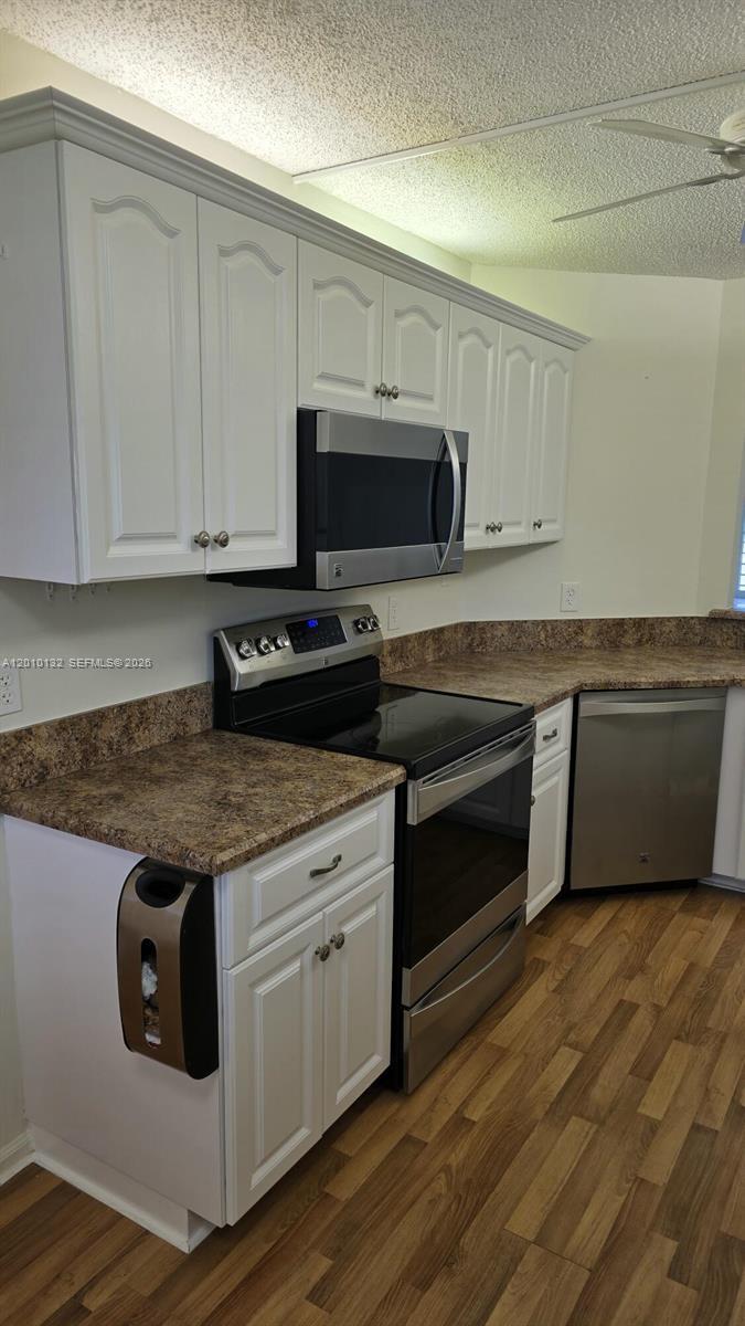 23305 Barwood Lane North, Unit 207 Boca Raton, FL 33428 - Photo 11 of 27 a kitchen with granite countertop a stove top oven a sink dishwasher and white cabinets with wooden floor