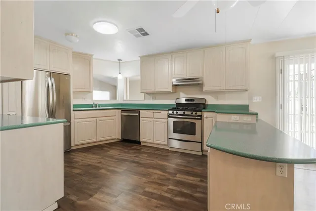 a kitchen with stainless steel appliances granite countertop a stove a sink a refrigerator white cabinets and wooden floor