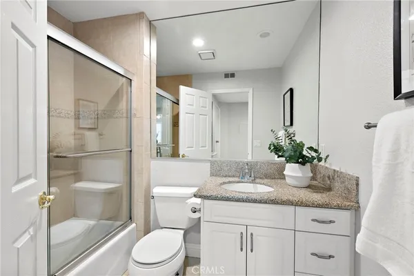 a bathroom with a granite countertop sink a toilet a mirror and shower