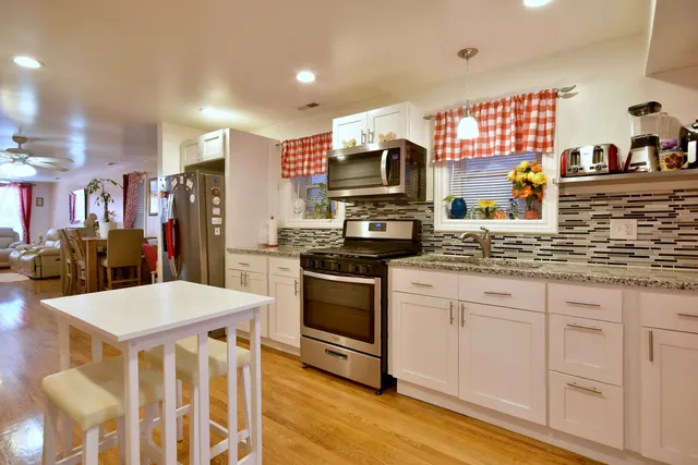 a kitchen with stainless steel appliances kitchen island granite countertop a refrigerator a stove a sink dishwasher and white cabinets with wooden floor