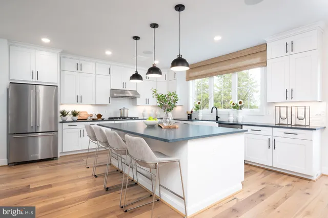 a kitchen with stainless steel appliances granite countertop a refrigerator a sink dishwasher a stove and white cabinets with wooden floor