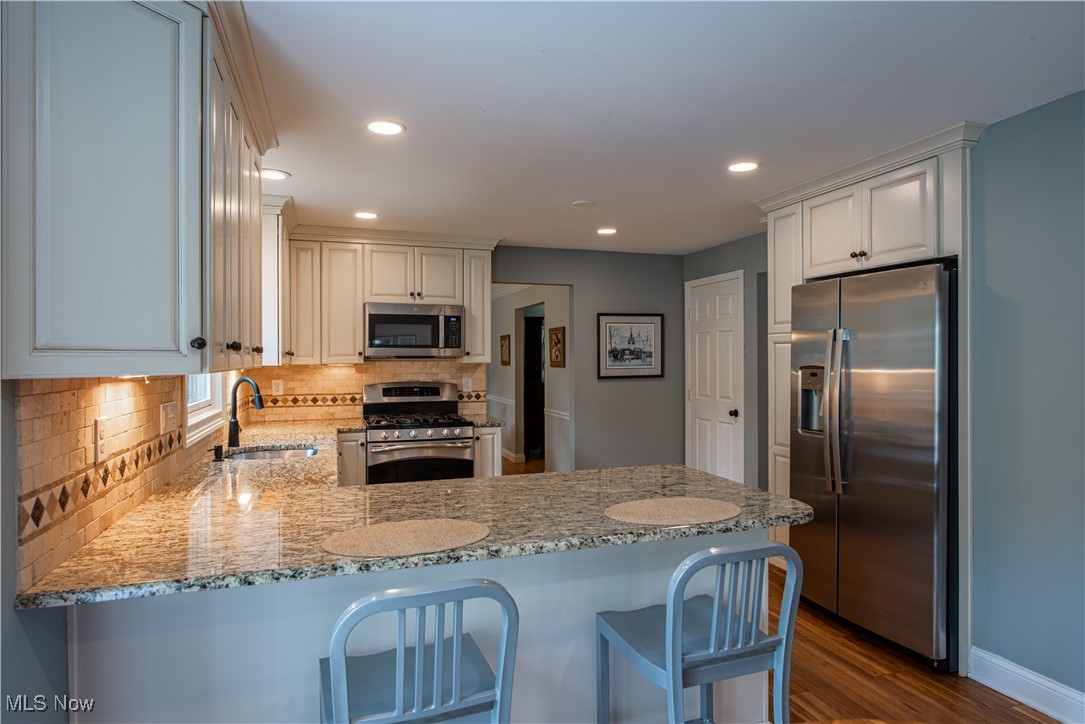 28314 Knickerbocker Road Bay Village, OH 44140 - Photo 11 of 38 Kitchen featuring backsplash, stainless steel appliances, dark hardwood / wood-style flooring, sink, and kitchen peninsula