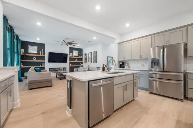 a kitchen with stainless steel appliances kitchen island granite countertop a stove top oven a sink dishwasher a refrigerator and white cabinets with wooden floor