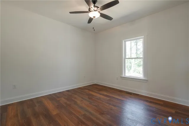 an empty room with wooden floor ceiling fan and windows