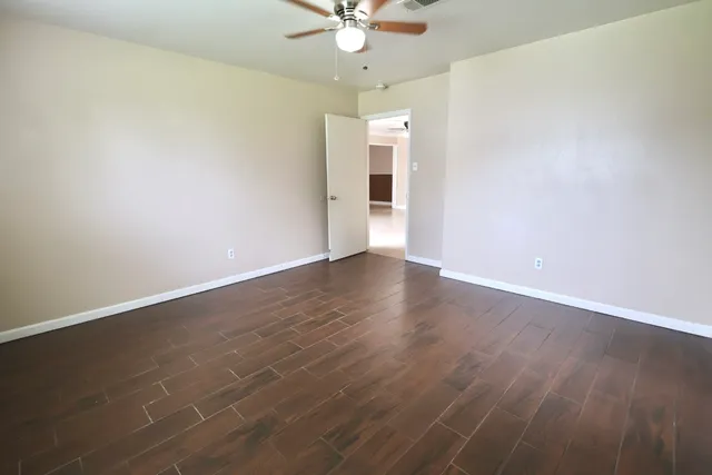 an empty room with wooden floor fan and windows