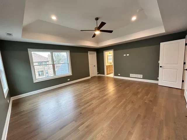 an empty room with wooden floor ceiling fan and windows