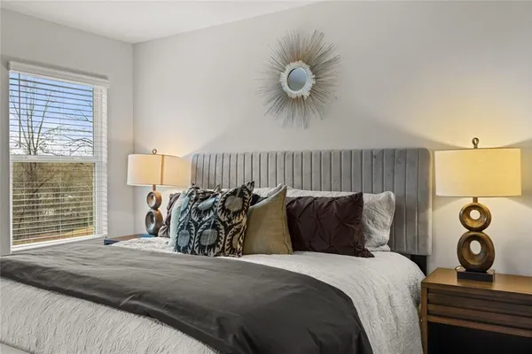 a white room with a white comforter and a painting on the wall