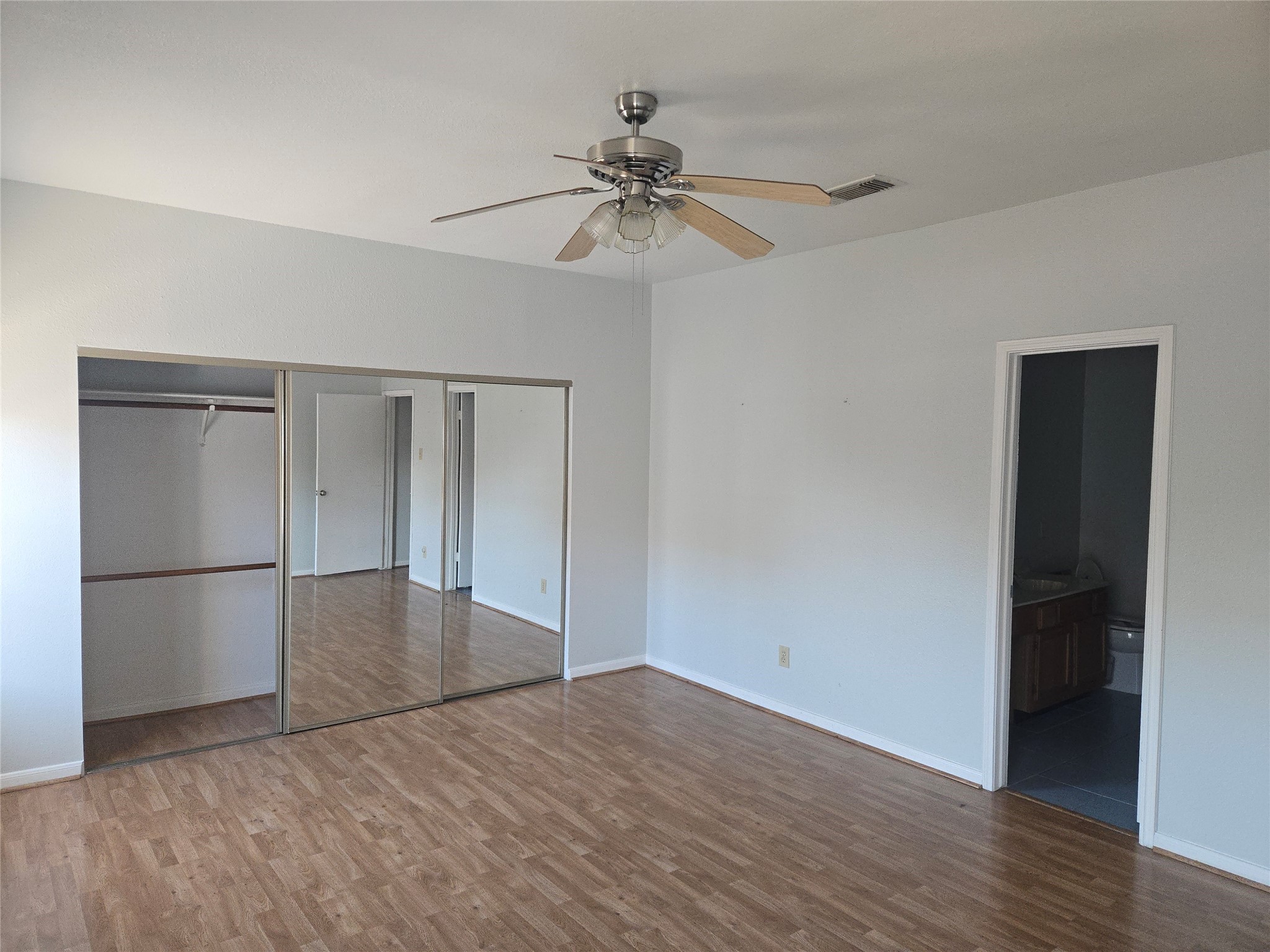 3780 Tanglewilde Street, Unit 501 Houston, TX 77063 - Photo 6 of 26 This spacious bedroom features laminate wood flooring, a ceiling fan, large mirrored closet doors, and an en-suite bathroom. The neutral walls provide a bright and airy feel, perfect for personalization.