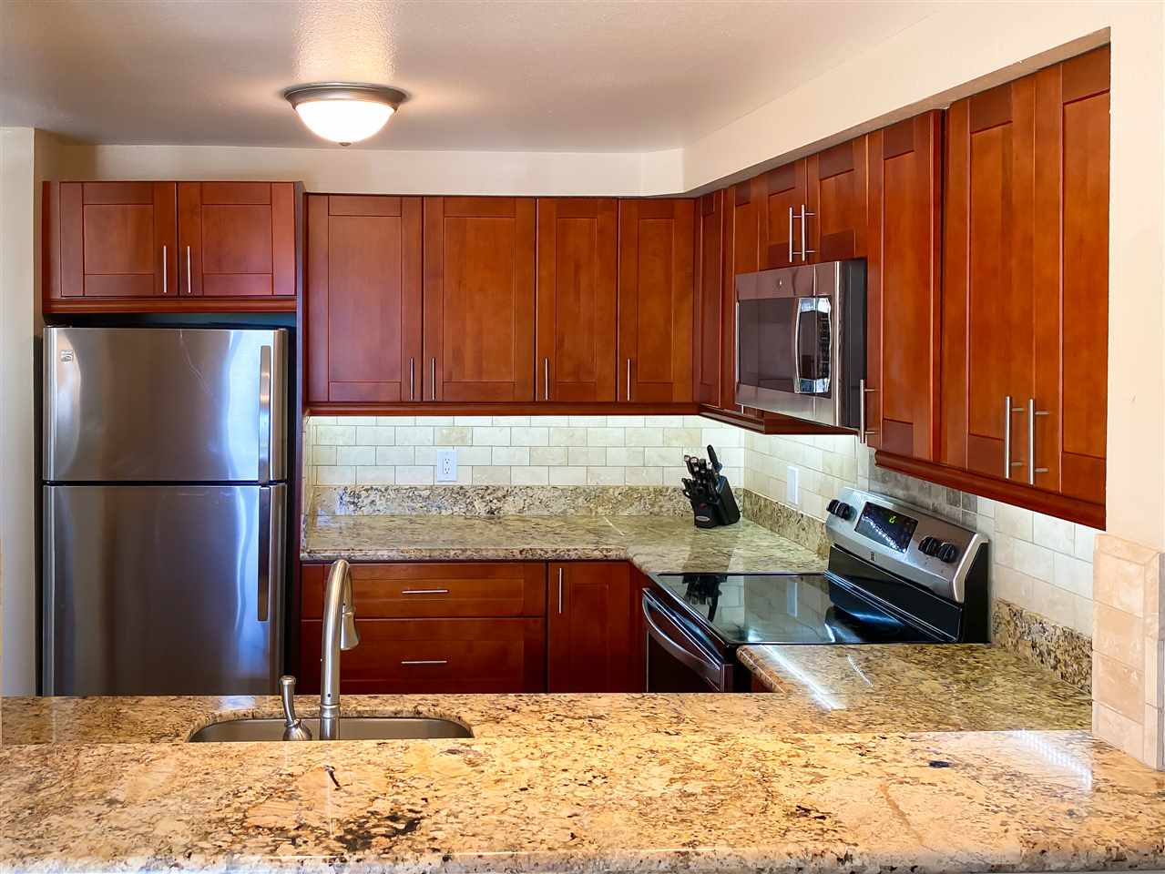 2747 South Kihei Road, Unit A201 Kihei, HI 96753 - Photo 5 of 29 a kitchen with stainless steel appliances granite countertop a refrigerator a stove and a sink with wooden cabinets