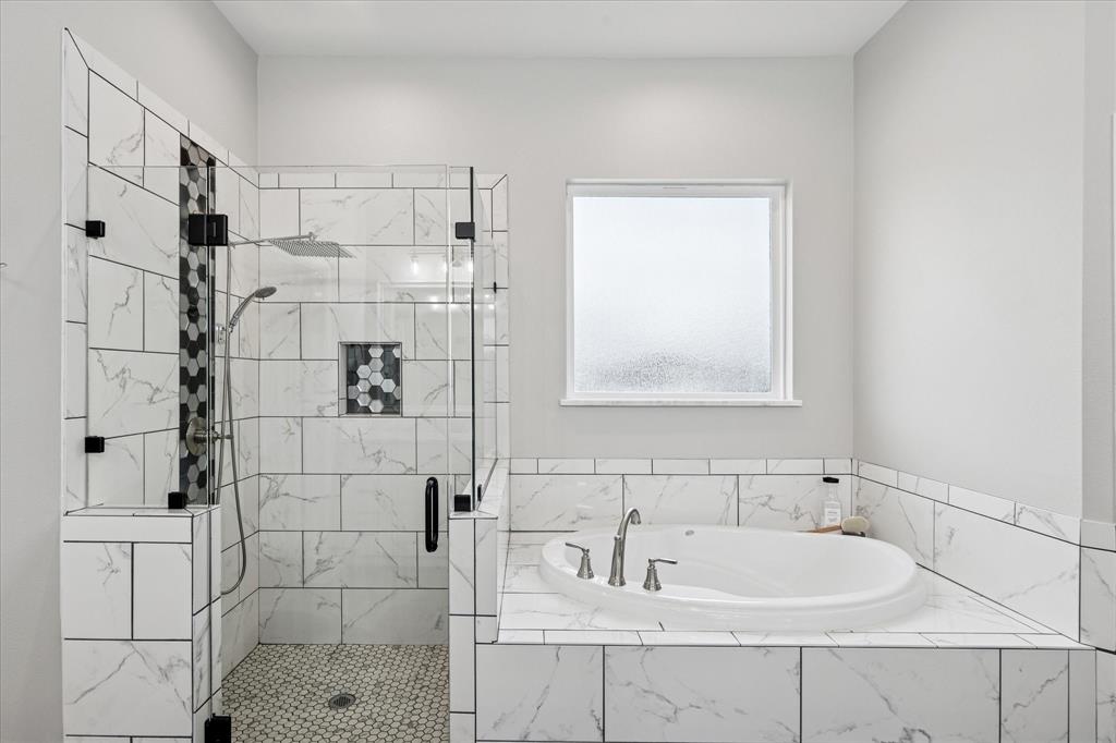 112 Friendship Way Boyd, TX 76023 - Photo 18 of 29 Contemporary bathroom featuring a spacious walk-in shower with clear glass enclosure and hexagon tile accents, a built-in soaking tub with deck-mounted fixtures, marble-look tile surround and wainscoting, and a frosted window