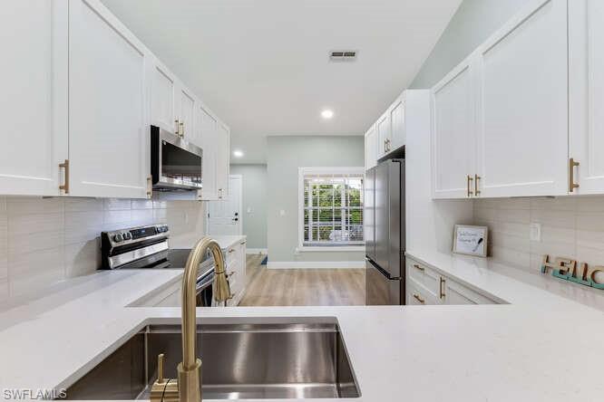 2876 West Crown Pointe Boulevard Naples, FL 34112 - Photo 3 of 36 Newly updated Kitchen with stainless steel appliances, white cabinetry, tile backsplash, hanging light fixtures, and lofted ceiling.