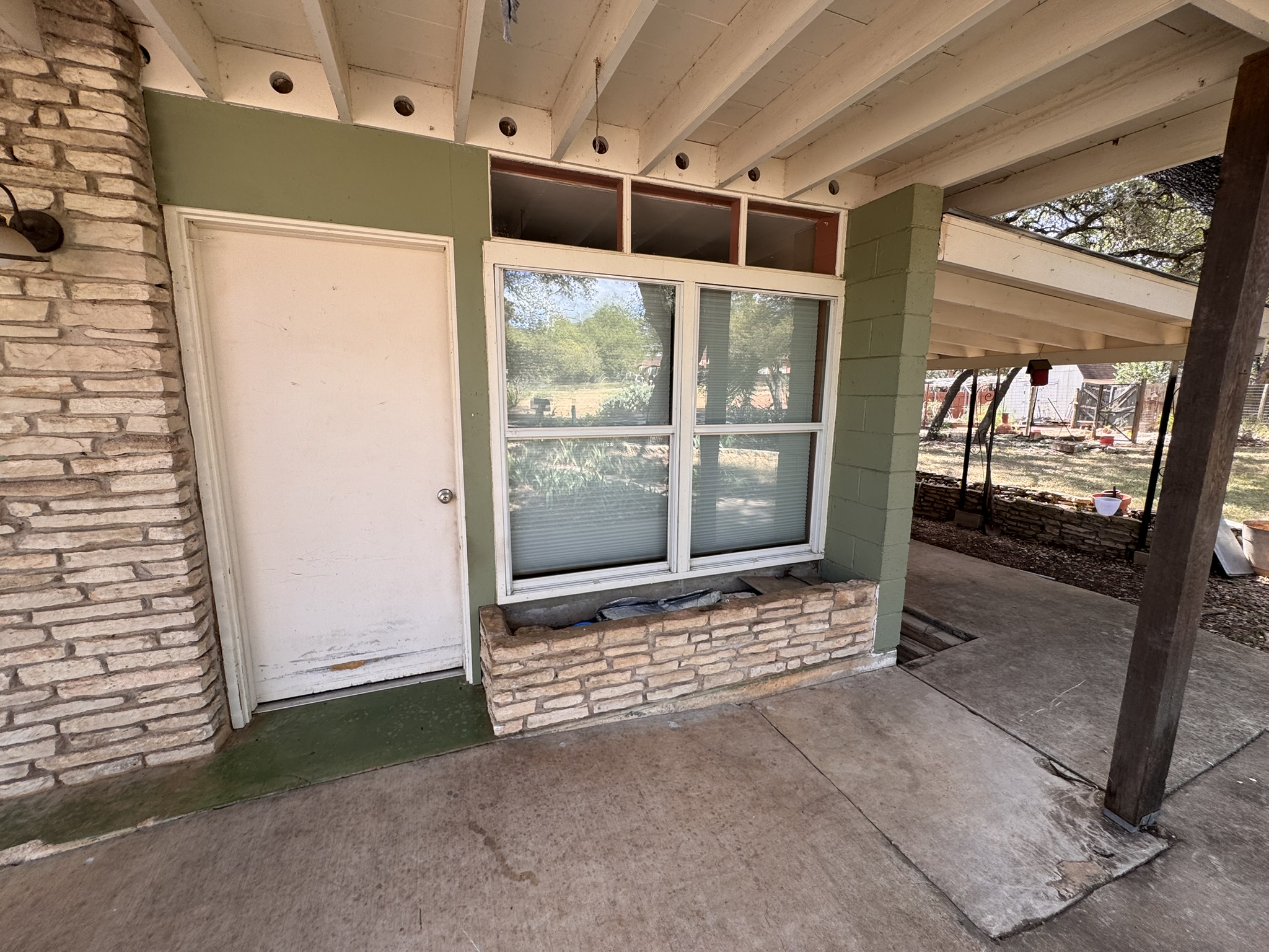 13 Presidio Road Wimberley, TX 78676 - Photo 6 of 7 A covered concrete patio area features midcentury-style stone detailing alongside exposed ceiling joists.