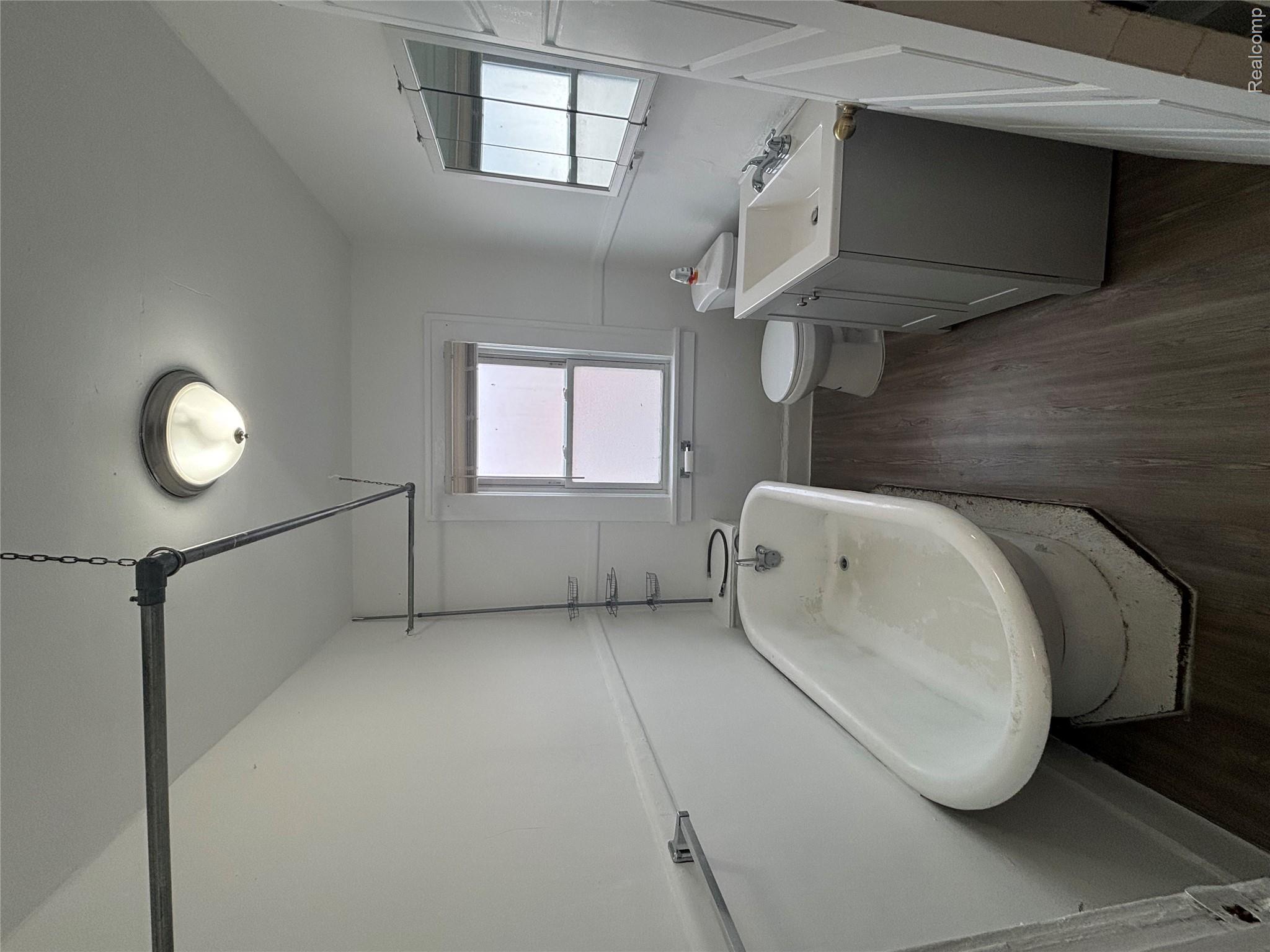 4740-4742 Alter Road Detroit, MI 48215 - Photo 19 of 20 Freestanding pedestal bathtub, single window with privacy glass, vanity with integrated sink, wood-finish flooring, and wall-mounted mirror