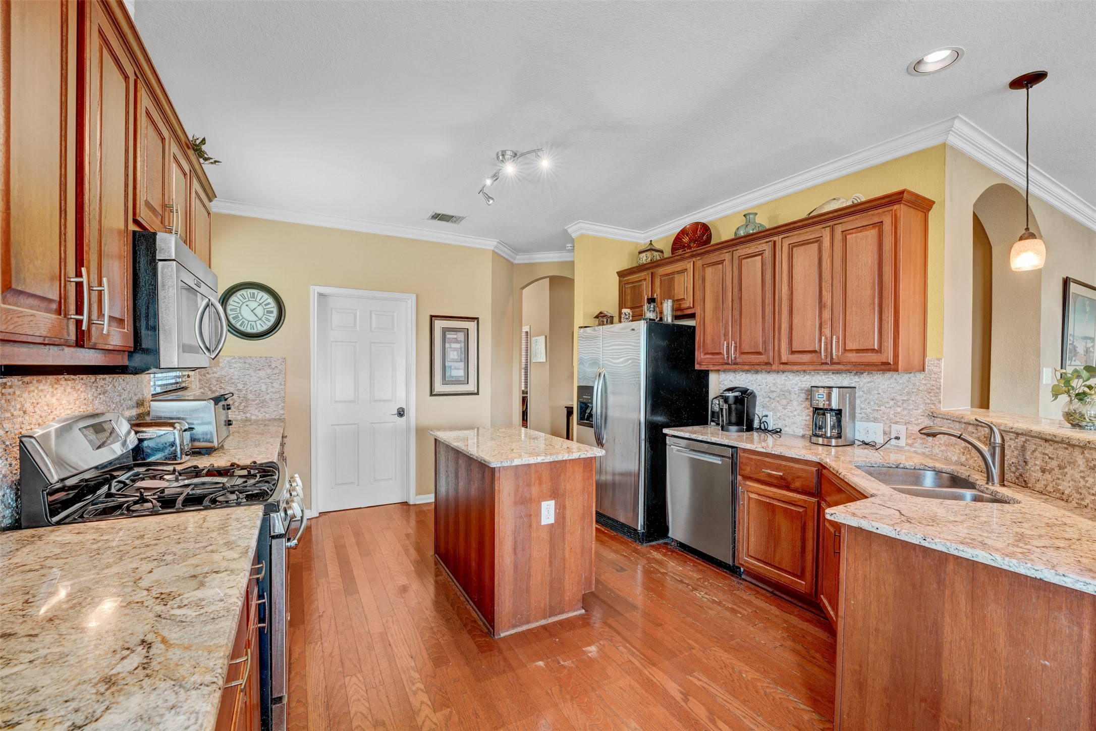 2521 Amen Corner Road Pflugerville, TX 78660 - Photo 8 of 40 Well-appointed kitchen featuring wood-finish flooring, abundant wood cabinetry, stone countertops, a center island, and stainless steel appliances