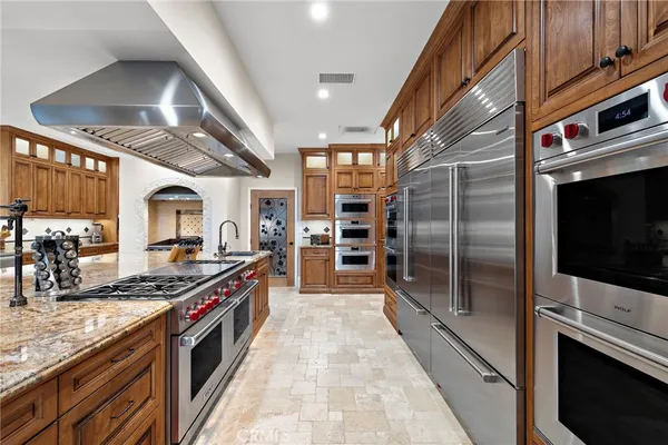 a large kitchen with stainless steel appliances granite countertop a large stove top oven a sink dishwasher and wooden cabinets with wooden floor