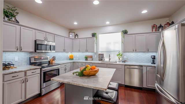 a kitchen with stainless steel appliances a sink a stove a refrigerator cabinets and wooden floor