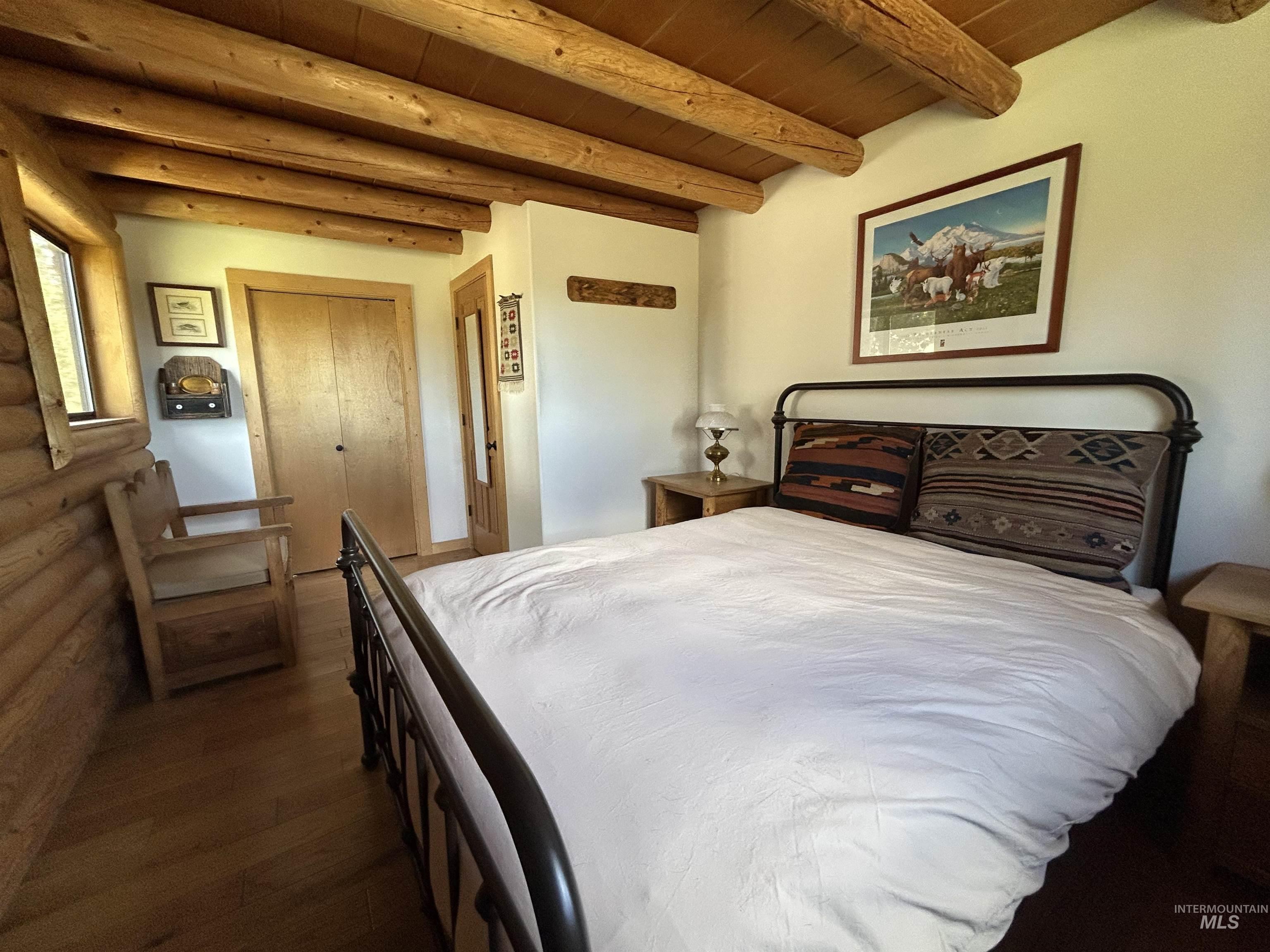 35 Sawtooth Way Stanley, ID 83278 - Photo 21 of 36 Bedroom featuring exposed wood beam ceiling, wood-finish flooring, log wall accents, and light wood bi-fold closet doors
