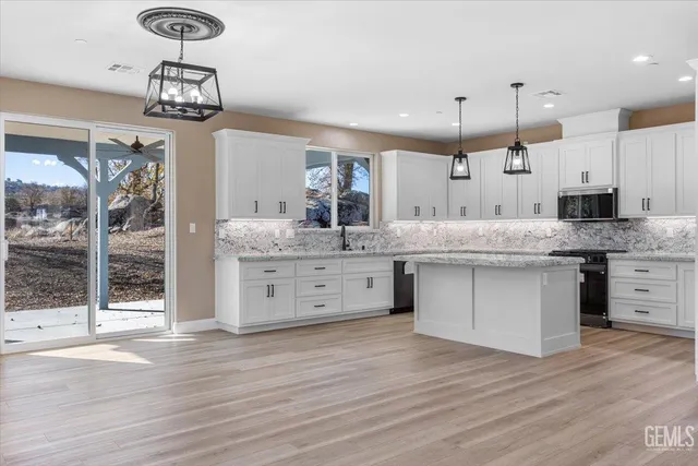 a kitchen with stainless steel appliances kitchen island granite countertop a stove a sink and white cabinets with wooden floor