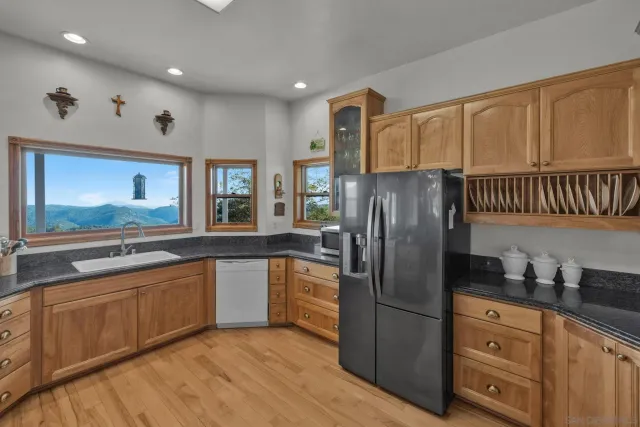 a kitchen with stainless steel appliances granite countertop a refrigerator a sink dishwasher and wooden cabinets with wooden floor