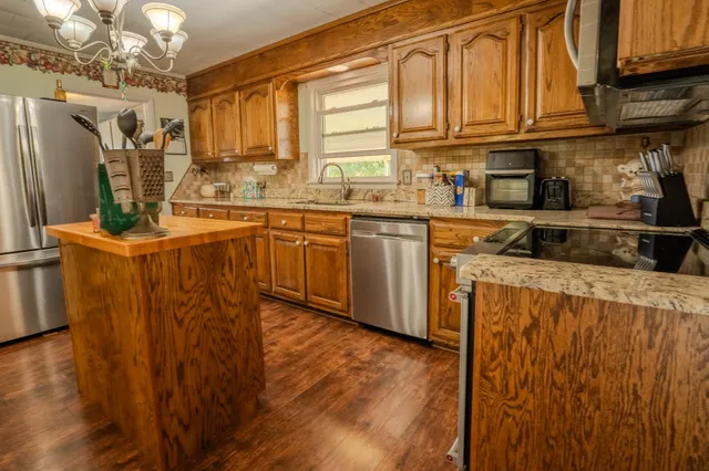 a kitchen with stainless steel appliances granite countertop a refrigerator a sink dishwasher and wooden cabinets with wooden floor