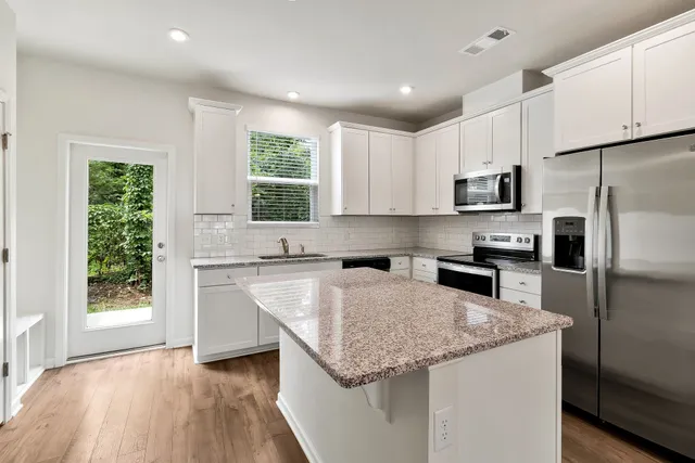 a kitchen with stainless steel appliances granite countertop a refrigerator a sink dishwasher a stove top oven a refrigerator and white cabinets with wooden floor