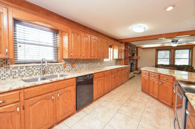 a large kitchen with kitchen island granite countertop a large counter top space a sink a window and stainless steel appliances