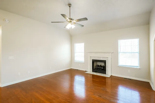 an empty room with wooden floor fireplace and windows