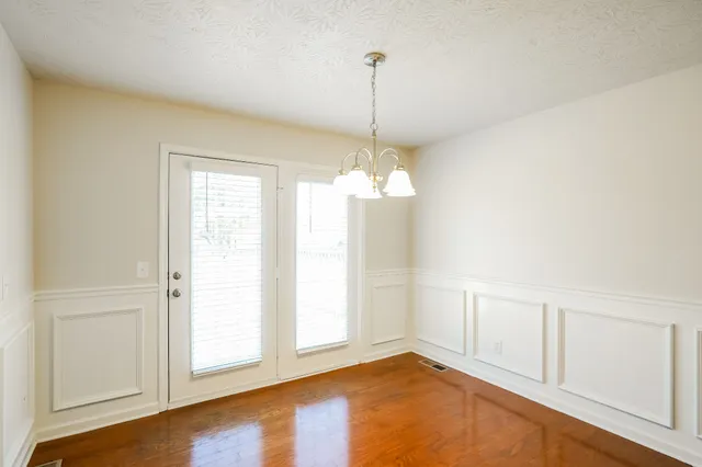 a view of an empty room with chandelier fan and kitchen view