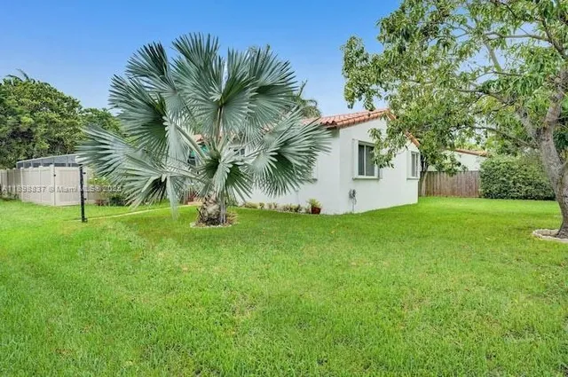 a view of a white house with a big yard and palm trees