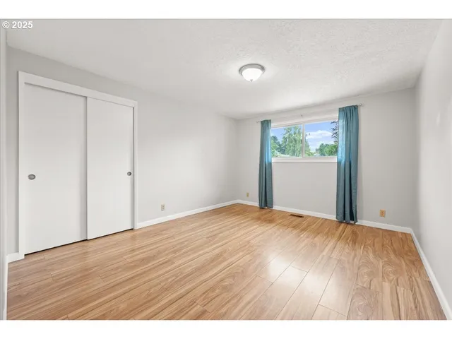 a view of an empty room with wooden floor and window