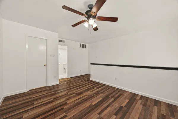 a view of an empty room with wooden floor and a ceiling fan