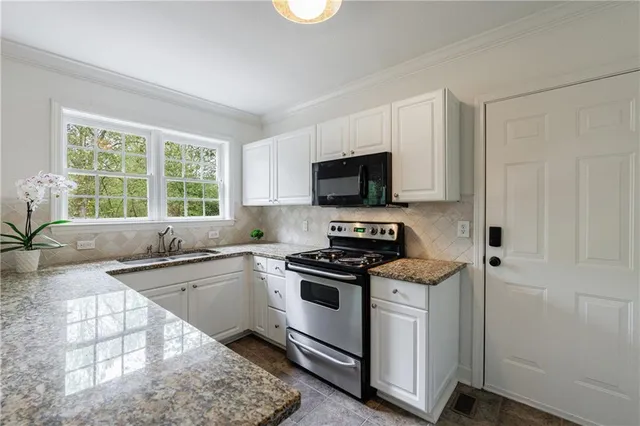 a kitchen with granite countertop white cabinets appliances and a window