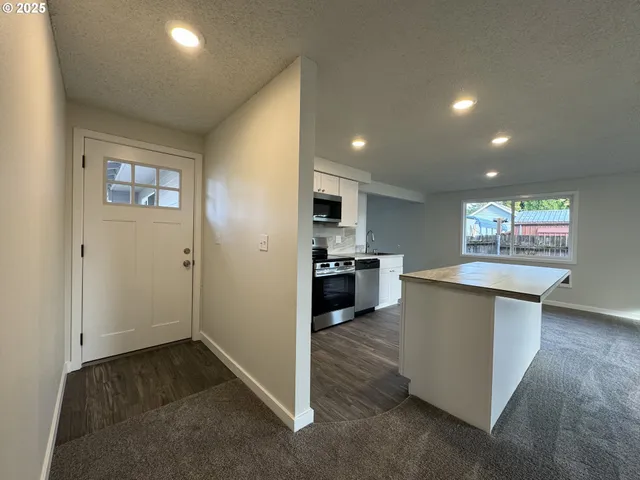 a living room with stainless steel appliances kitchen island granite countertop a refrigerator and a stove top oven
