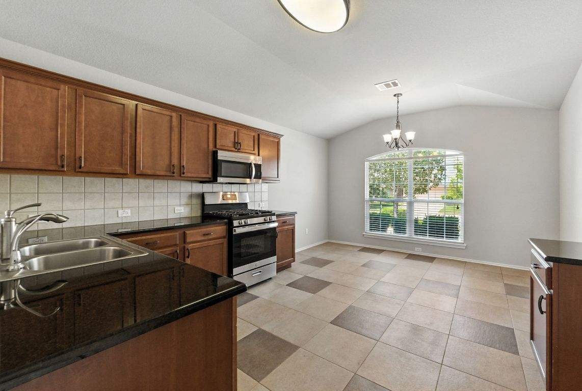 2840 Hearthsong Loop Round Rock, TX 78665 - Photo 9 of 39 a kitchen with granite countertop a stove a sink dishwasher and a microwave oven with white cabinets