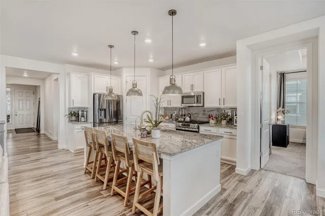 a kitchen with stainless steel appliances granite countertop a kitchen island a stove a refrigerator a sink a dining table and chairs with wooden floor