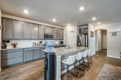 a kitchen with stainless steel appliances granite countertop a refrigerator a sink dishwasher a stove and white cabinets with wooden floor